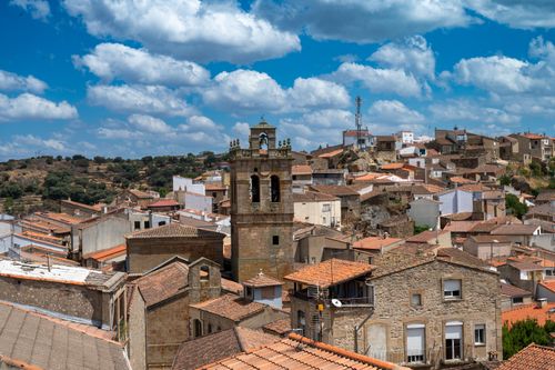 Free Picturesque view of a traditional Spanish village under a vibrant blue sky with scattered clouds. Stock Photo
