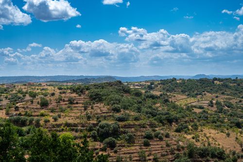 Free A picturesque view of lush rolling hills under a clear blue sky with fluffy clouds. Stock Photo