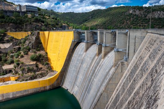 A breathtaking view of a hydroelectric dam set against a lush, green landscape and a blue sky.