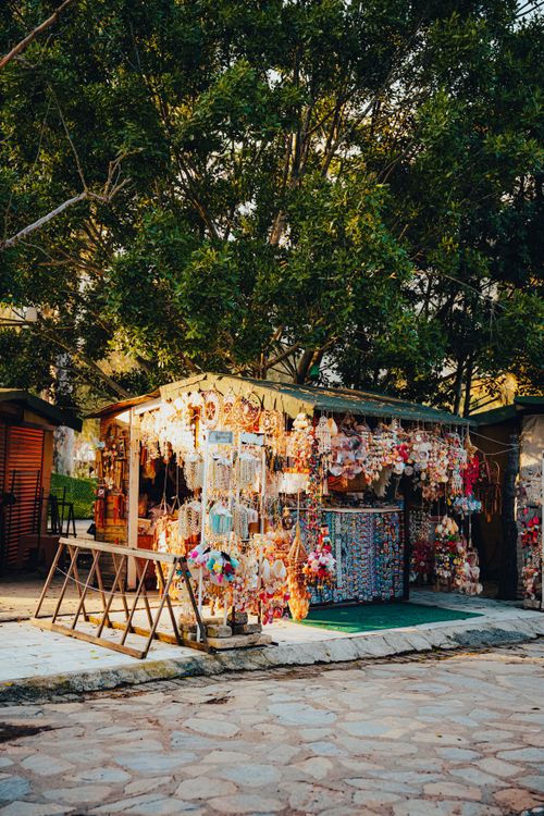 Free Outdoor market stall selling colorful souvenirs under leafy trees during daylight. Stock Photo