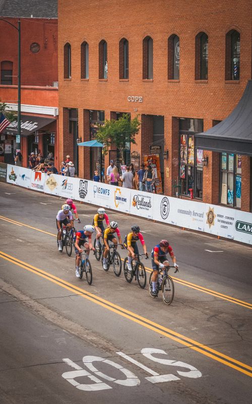 Free Cyclists racing in city streets with spectators and historic brick buildings. Stock Photo