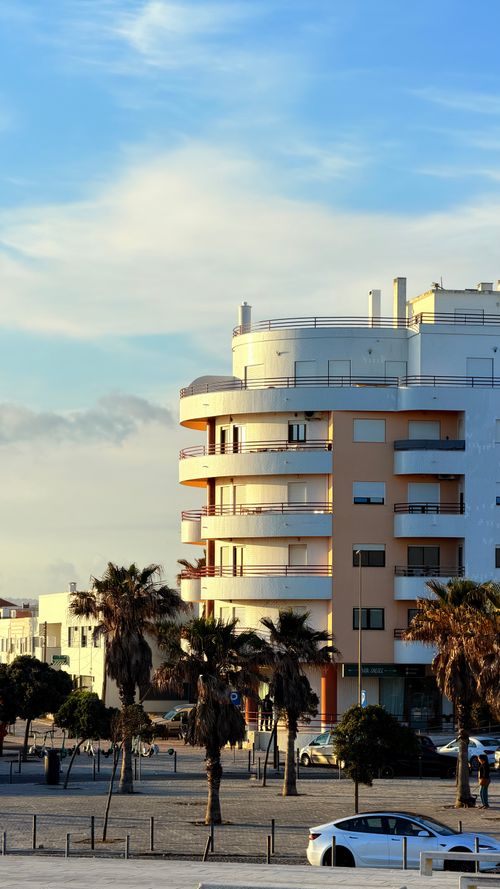 Free Contemporary coastal apartment building with palm trees under a vibrant evening sky. Stock Photo