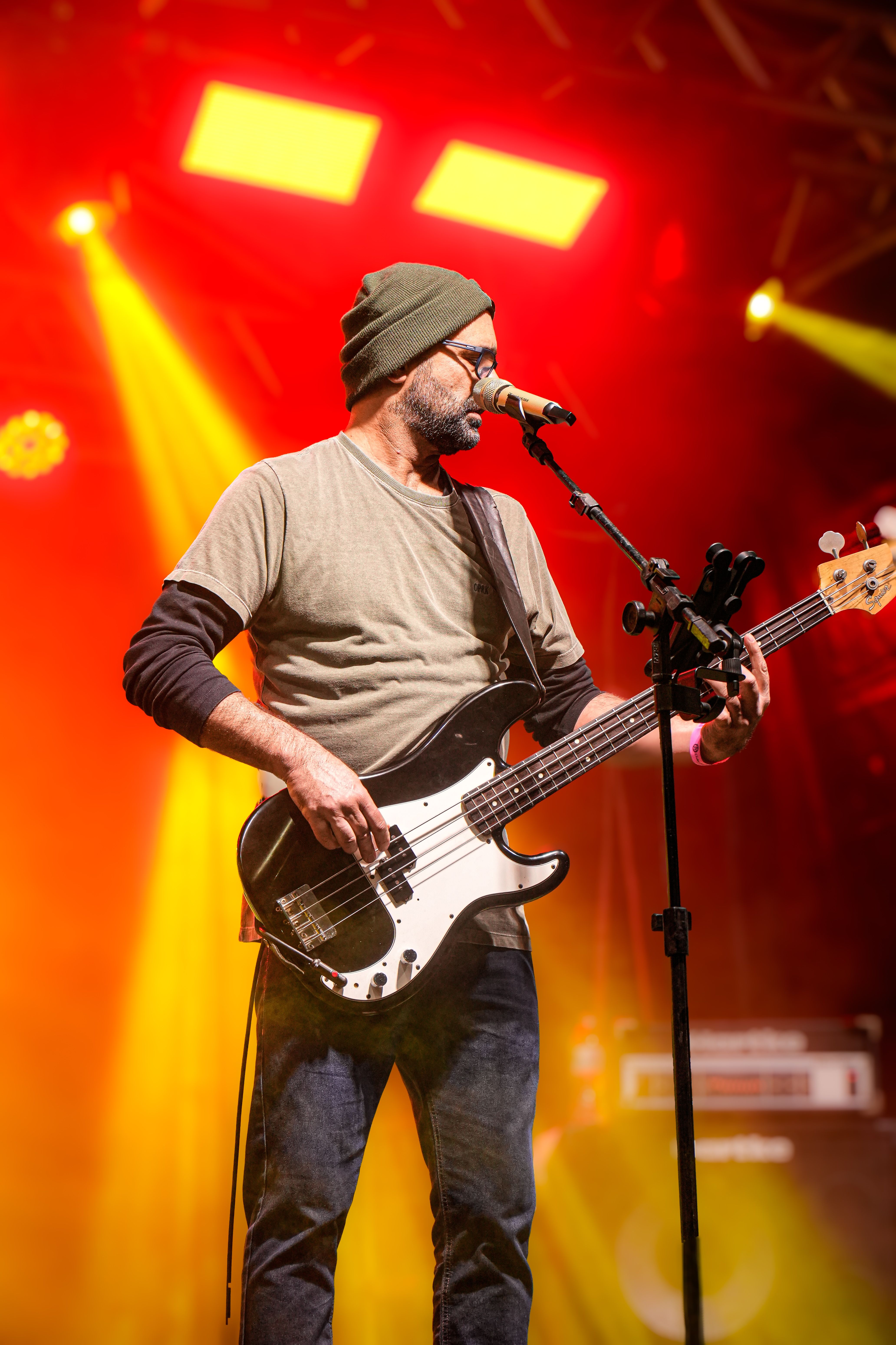 A musician passionately plays bass guitar under vibrant stage lights at night.