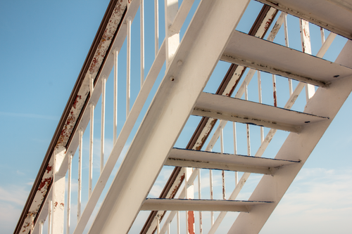 Free Close-up of an old metal staircase with peeling paint under a clear blue sky. Stock Photo