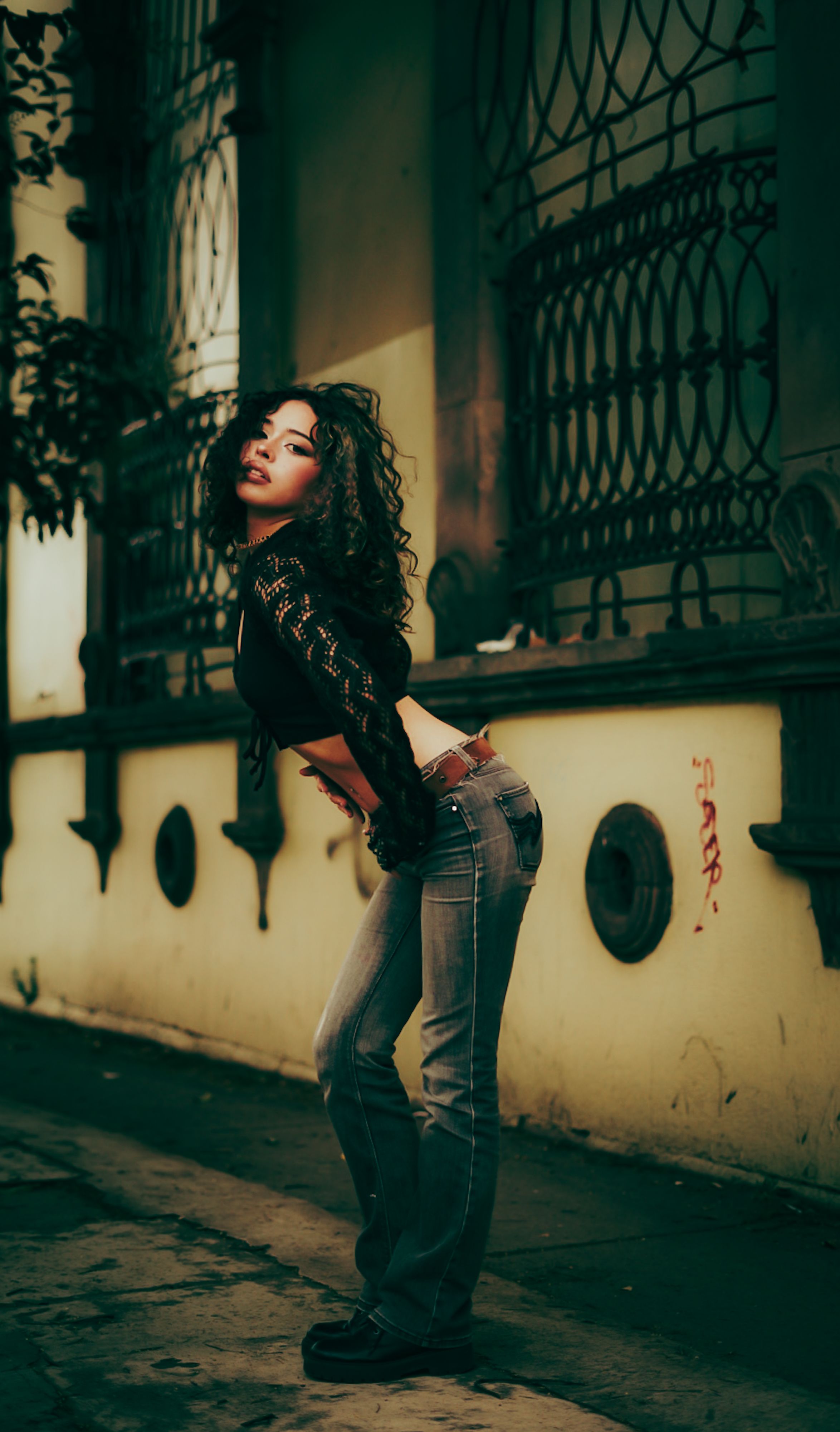 Woman in trendy attire poses on a city street with vintage architecture.