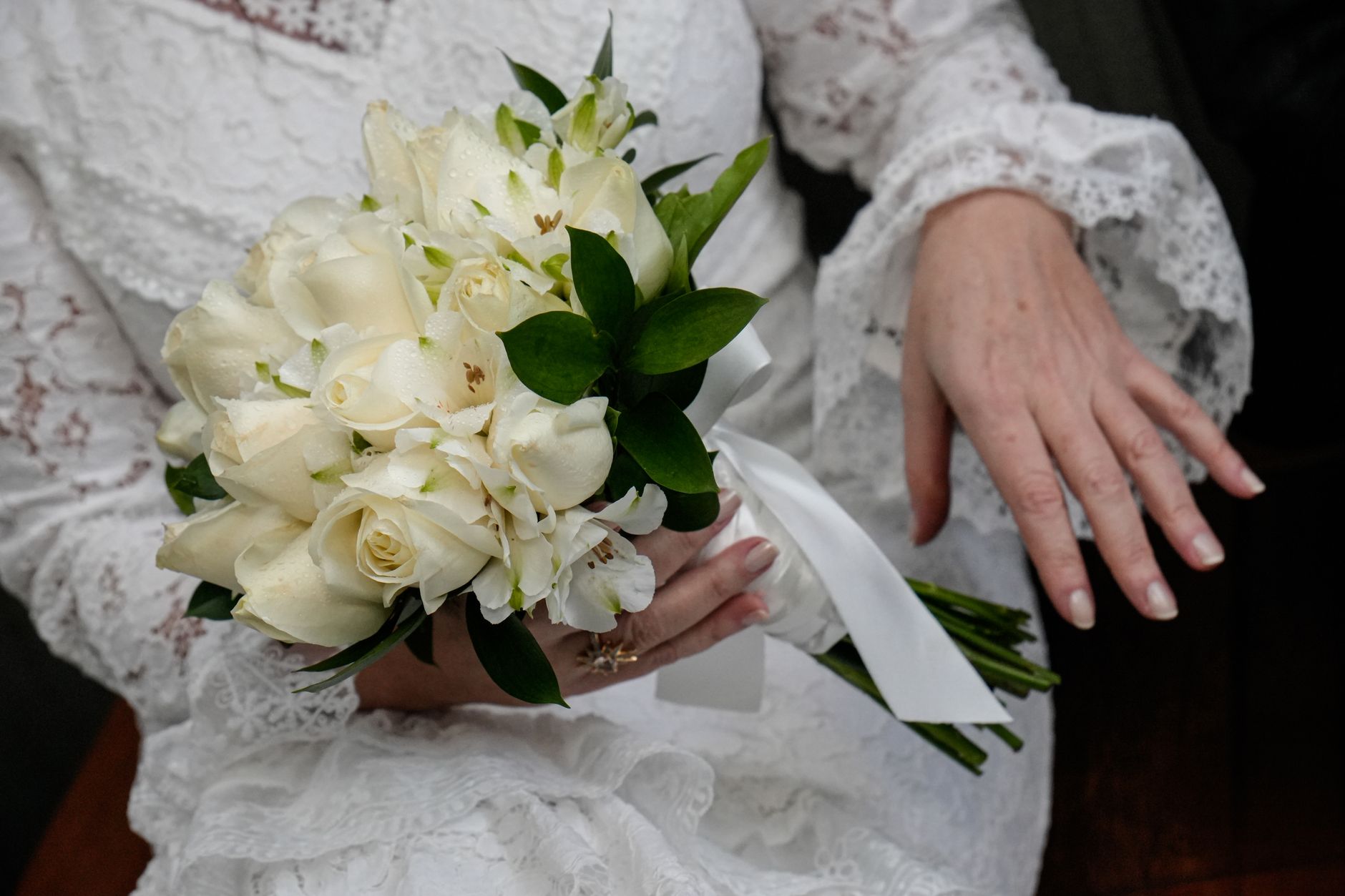 Close-up of a bride in lace dress holding an ivory rose bouquet with delicate details.