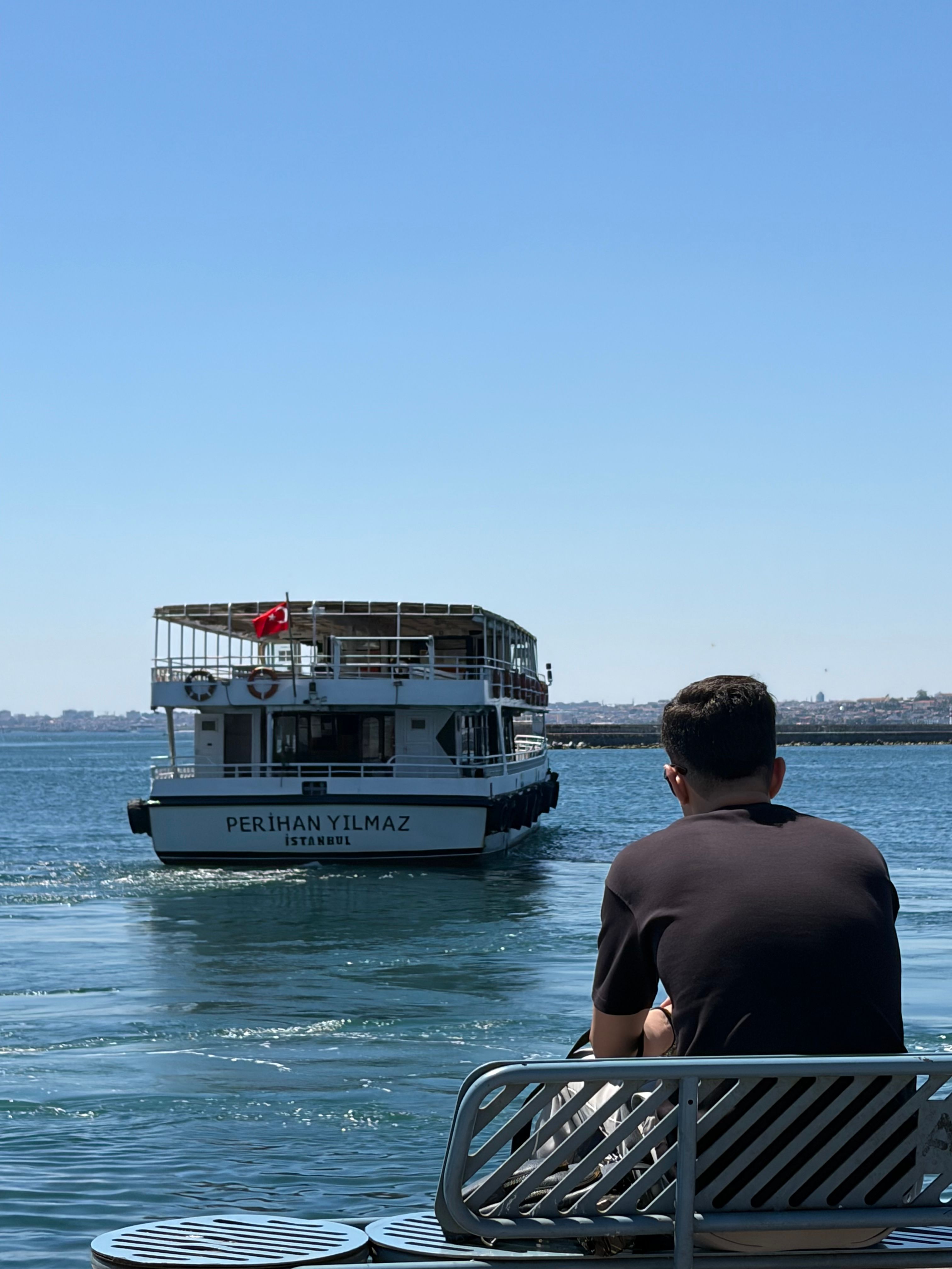 A man sits by the Istanbul waterfront watching a ferry named Perihan Yılmaz.