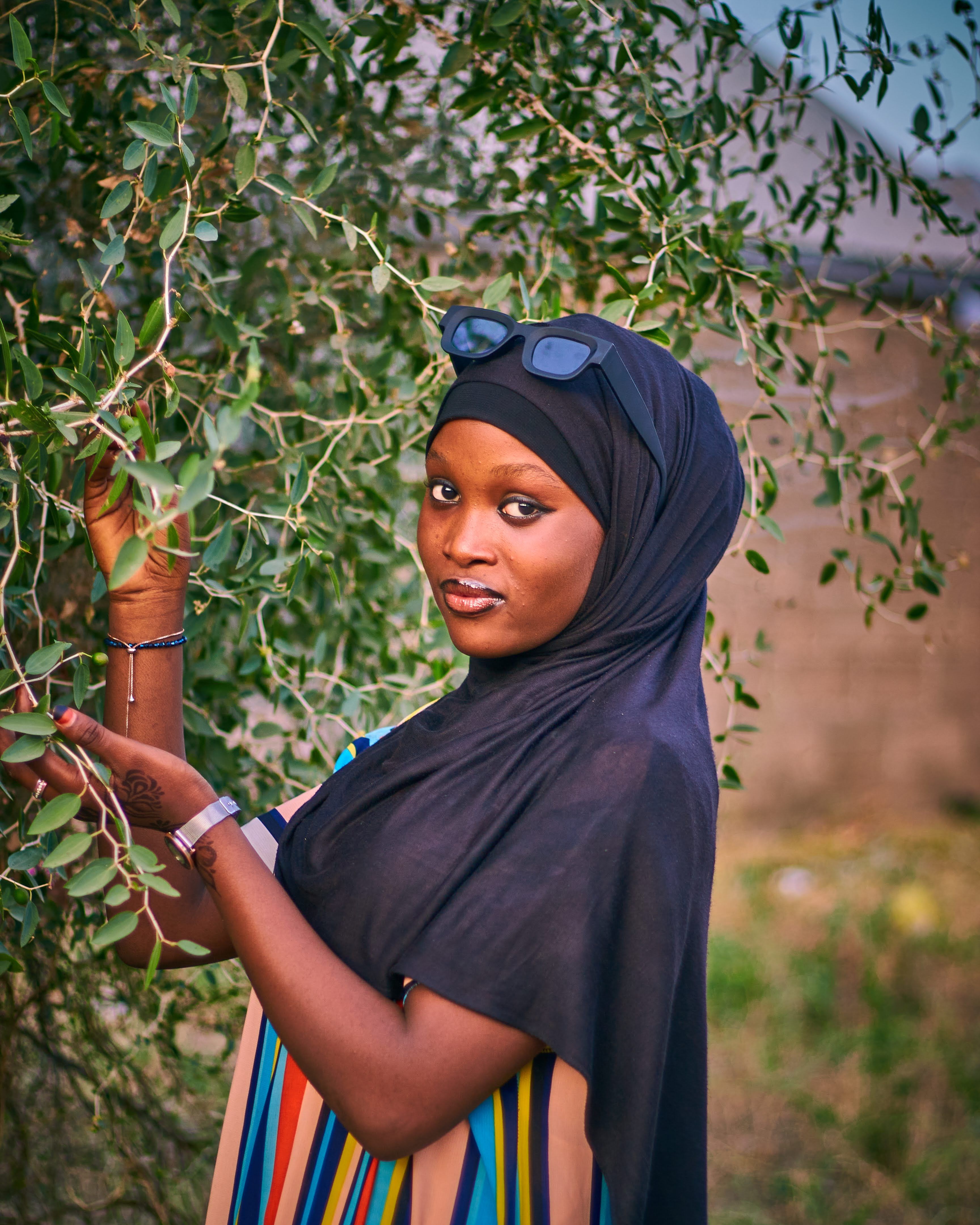 A woman wearing a hijab and sunglasses poses gracefully outdoors among lush greenery in Abuja, Nigeria.