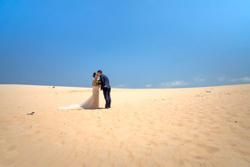 Free Elegant couple shares a romantic kiss on a desert landscape under a bright blue sky. Stock Photo
