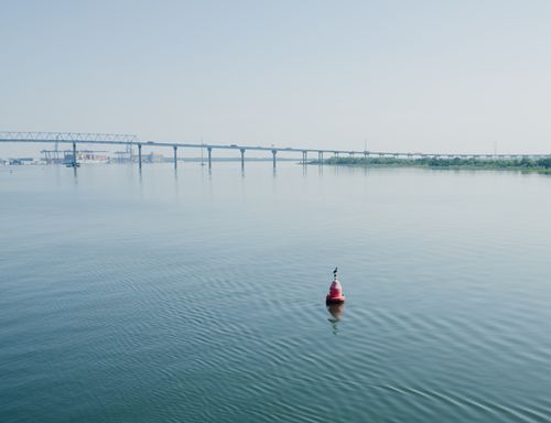 Free Peaceful image of a bridge spanning a calm river with a buoy and clear sky, perfect for travel or nature themes. Stock Photo