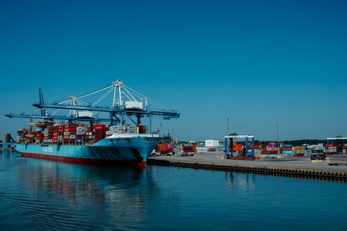 Free Impressive view of a large container ship at an industrial port with cranes and containers under a clear blue sky. Stock Photo