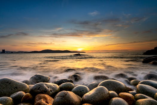 A serene sunset over a rocky seashore with a dramatic sky and calm ocean waves.