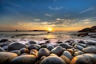 宁静的岩石海岸景观具有惊人的日落在海洋与戏剧性的云