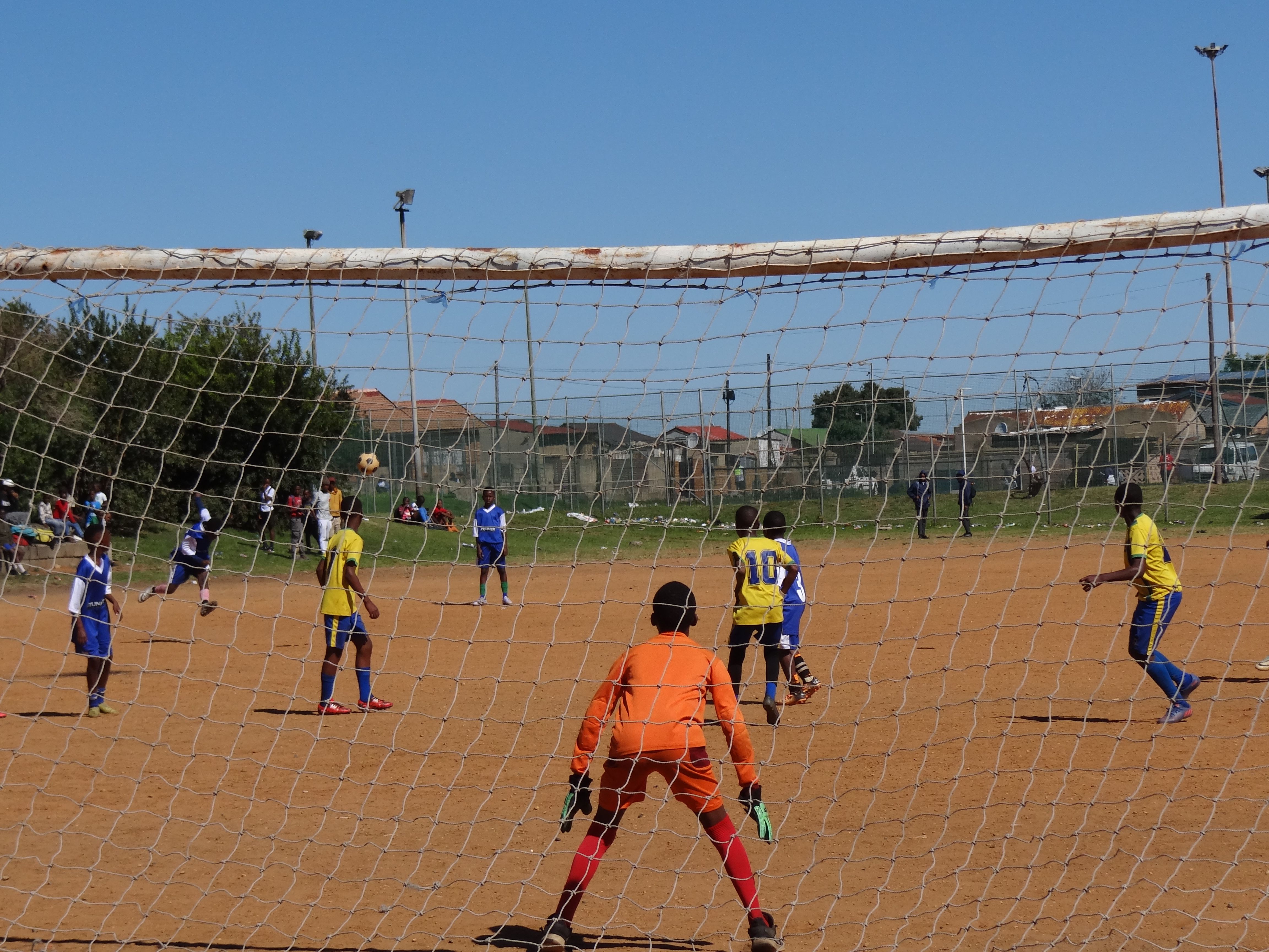 Action shot of youth soccer game in Johannesburg, focused on goalie defending the net.