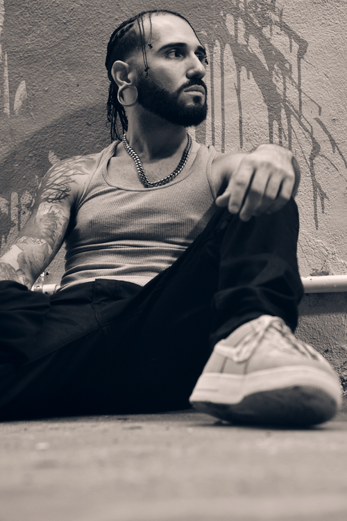 Free A tattooed man with piercings sits against a graffiti wall wearing casual attire. Stock Photo