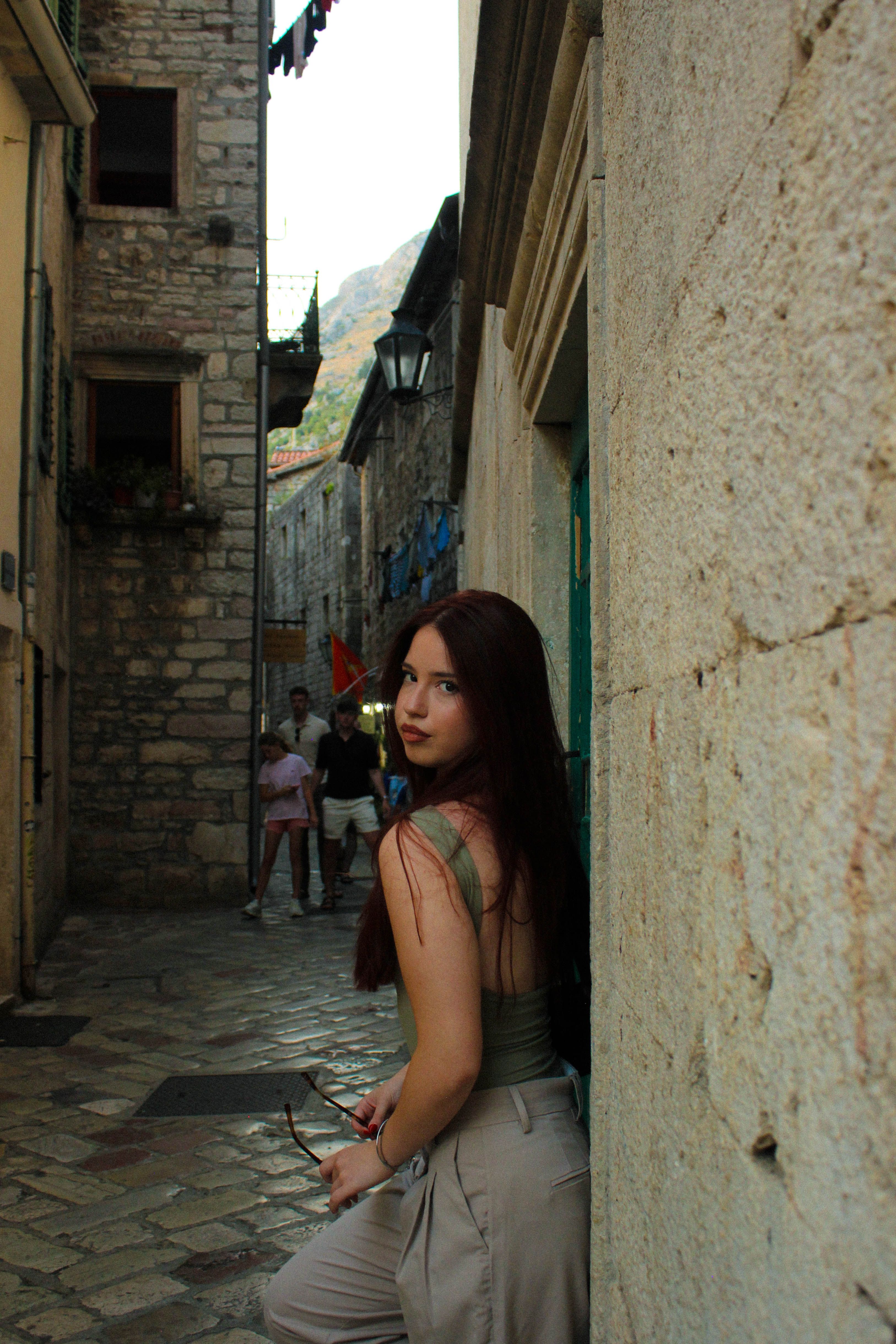 A young woman stands in a narrow stone alleyway of a historic town, exuding a timeless charm.