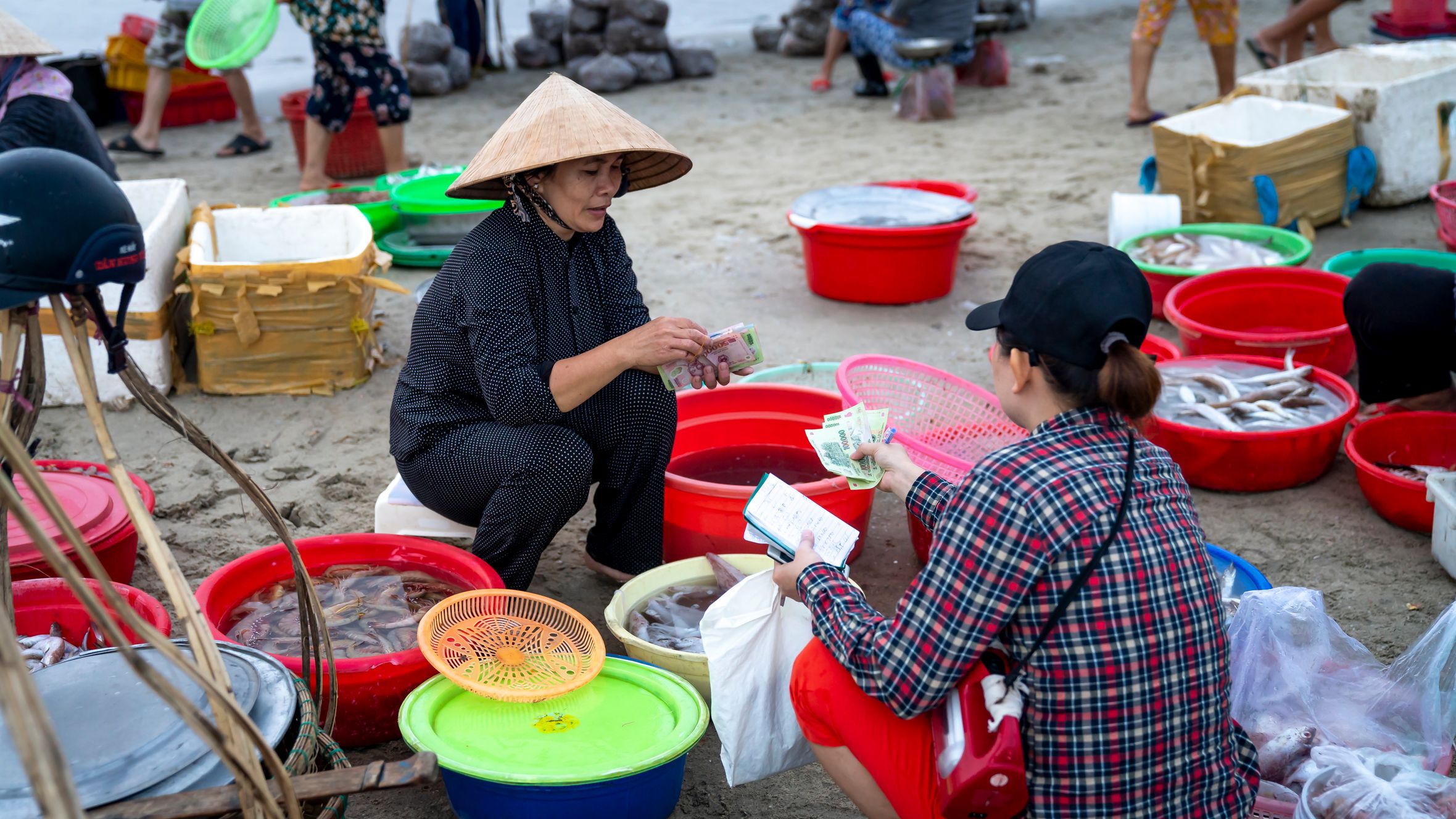 Lively beachside fish market with vendors and buyers engaged in seafood transactions.