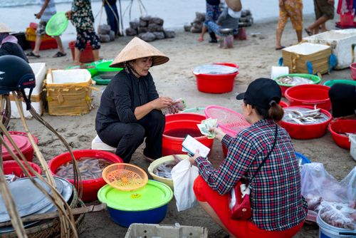 Free Lively beachside fish market with vendors and buyers engaged in seafood transactions. Stock Photo