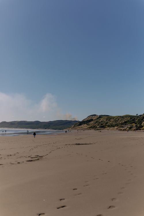 Free Serene beach scene with footprints and people strolling on a sunny day, capturing natural beauty and relaxation. Stock Photo