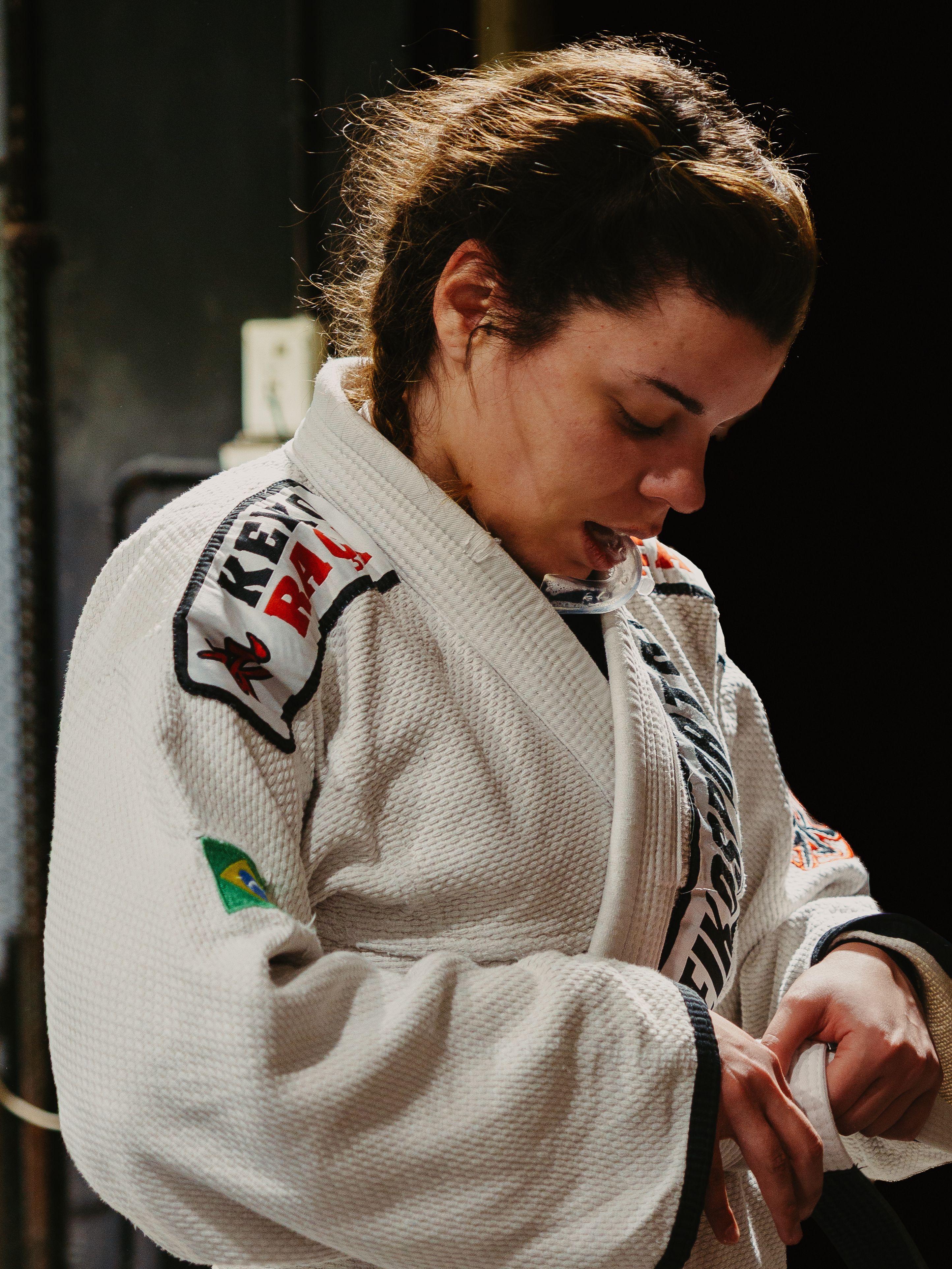 A focused female martial artist adjusting her gi before Brazilian Jiu-Jitsu training.