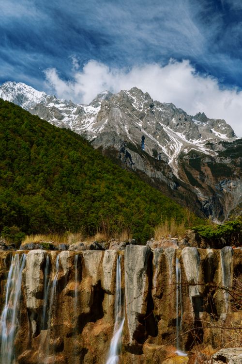 Free Stunning view of a mountain range with cascading waterfalls and lush forest. Stock Photo