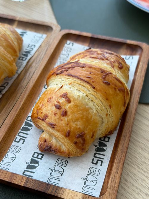 Free Golden cheese croissant served on a stylish wooden tray, perfect for a breakfast setting. Stock Photo