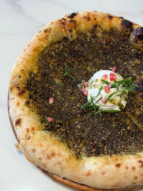 Free Freshly baked man'ousheh topped with za'atar, creamy labneh, herbs, and pomegranate seeds. Stock Photo