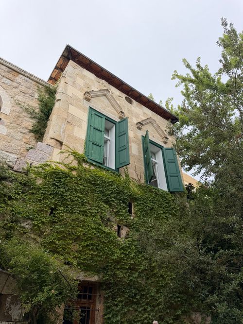 Free Charming vintage stone house with green shutters and lush ivy in a serene setting. Stock Photo