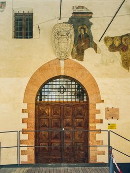 Ancient wooden door with frescoes and coat of arms on a historic building in Assisi, Italy.