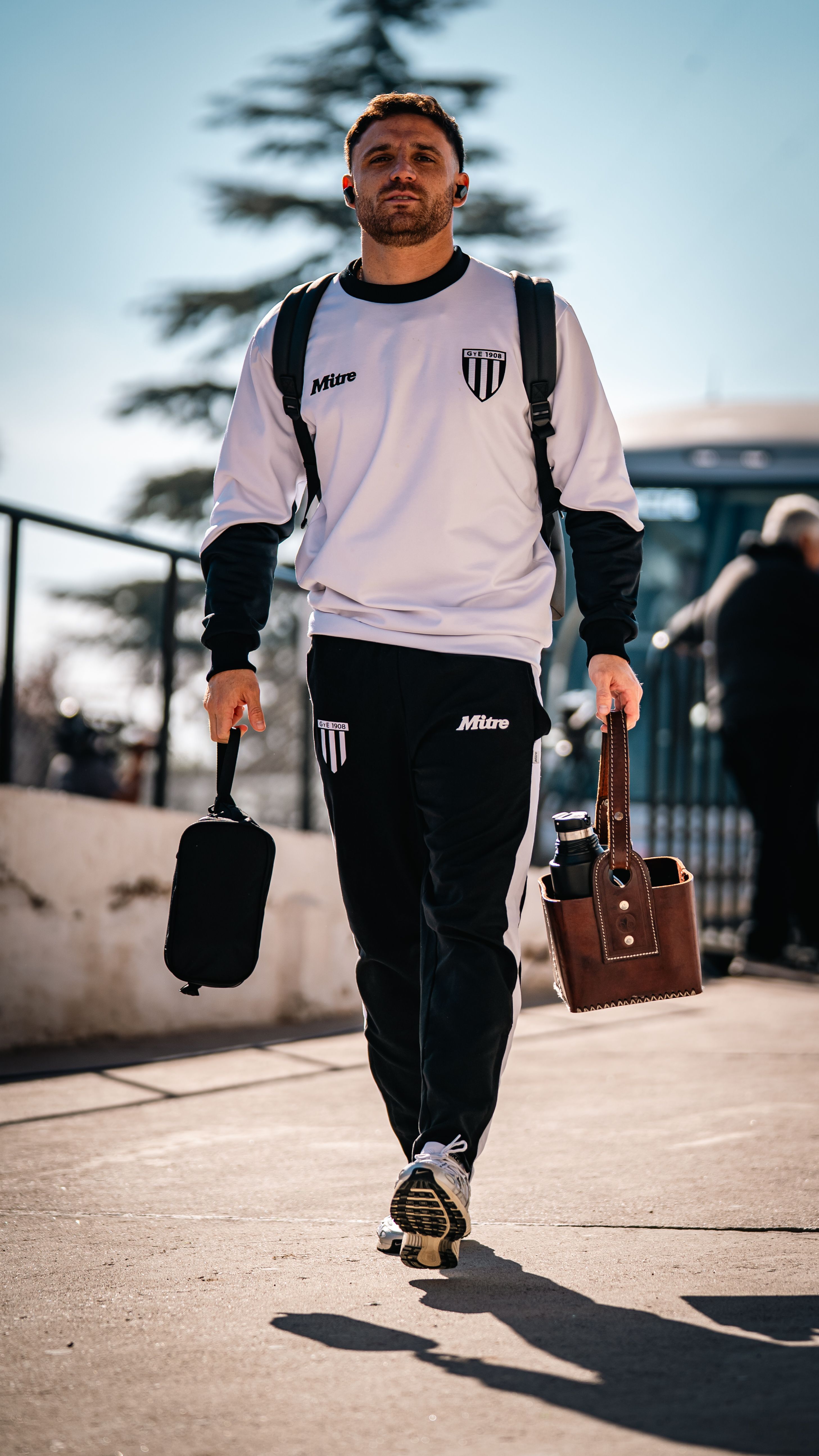 Young male athlete walking outdoors in sports gear carrying bags.