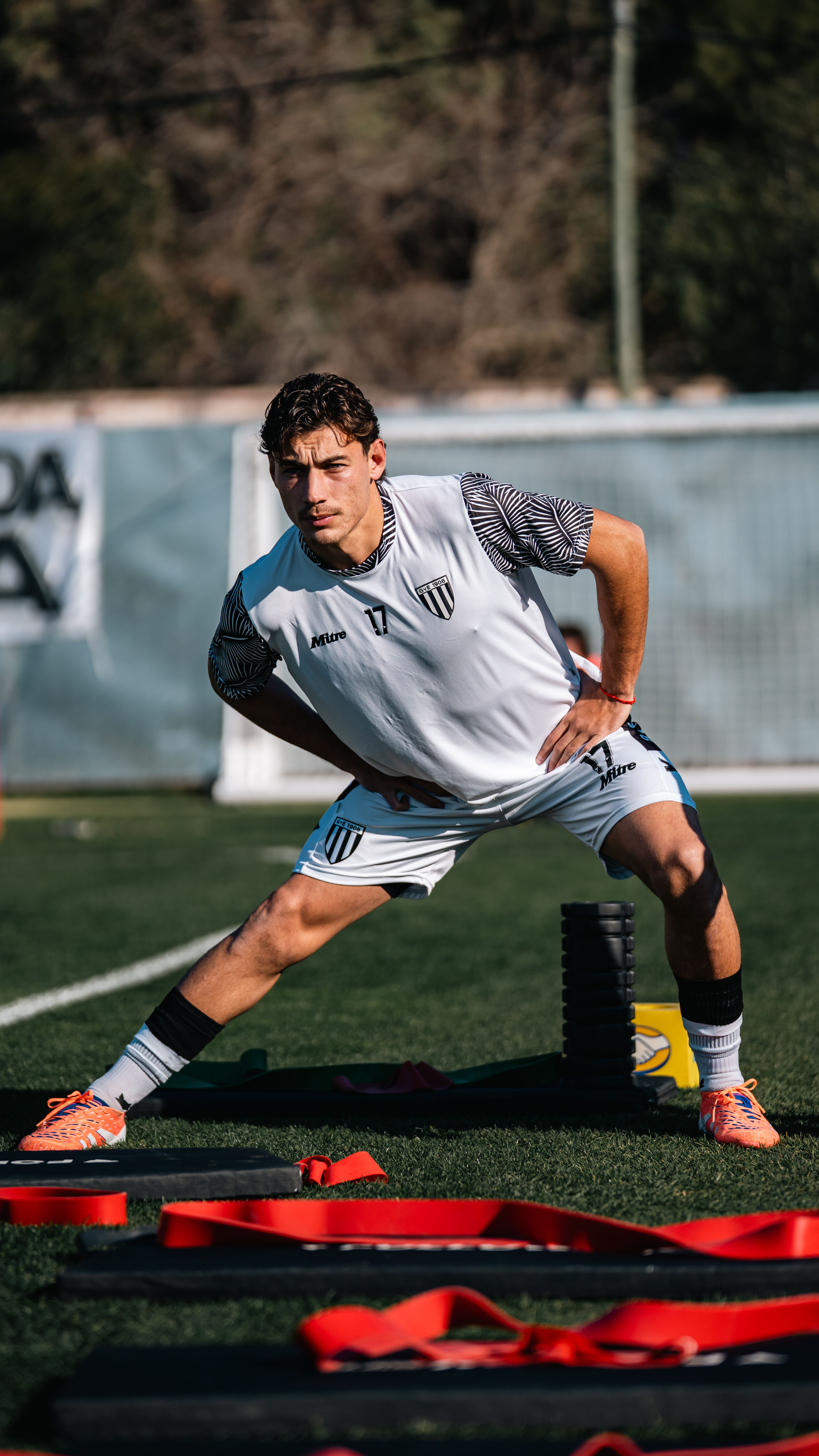 A male soccer player stretching during a training session on an outdoor field.