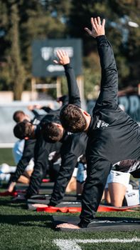 A group of athletes perform stretching exercises on a field outdoors. Fitness and teamwork concept.