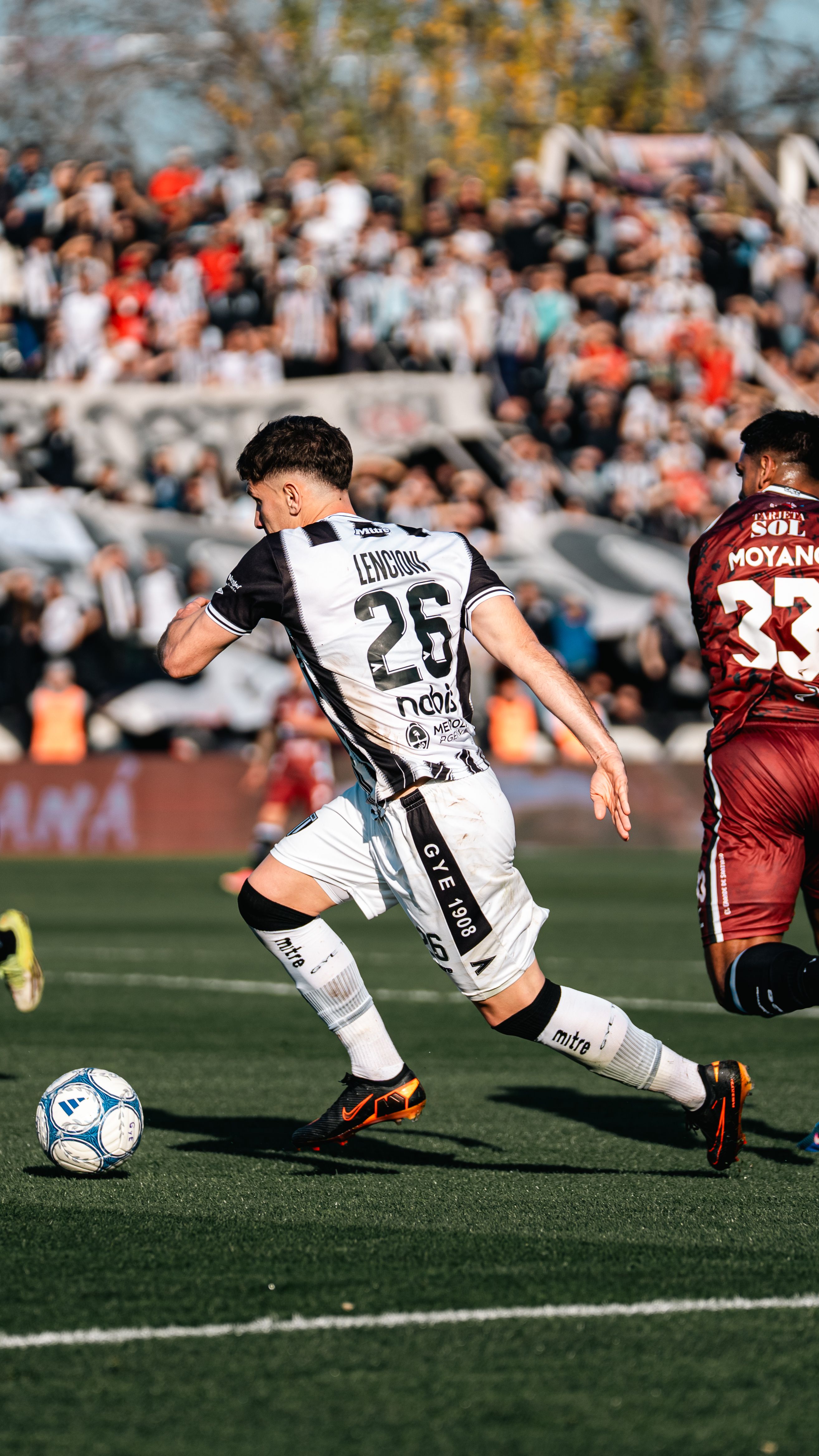 Exciting action shot of soccer players competing on a sunny day with a lively crowd in the background.