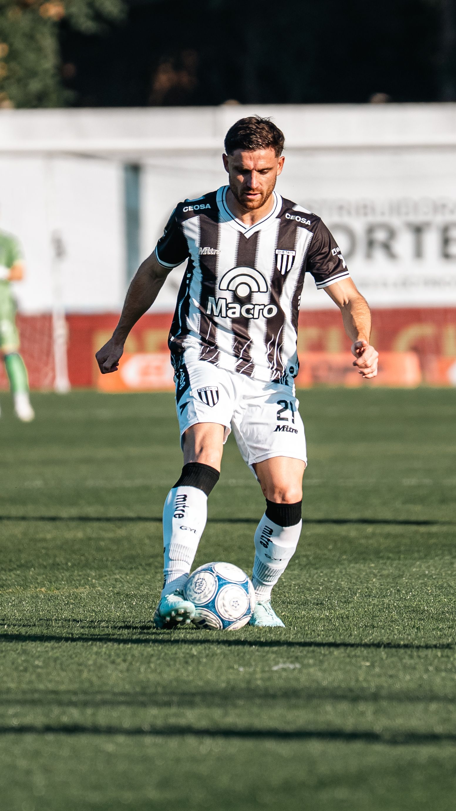 Male soccer player in action, dribbling during a match outdoors in daylight.