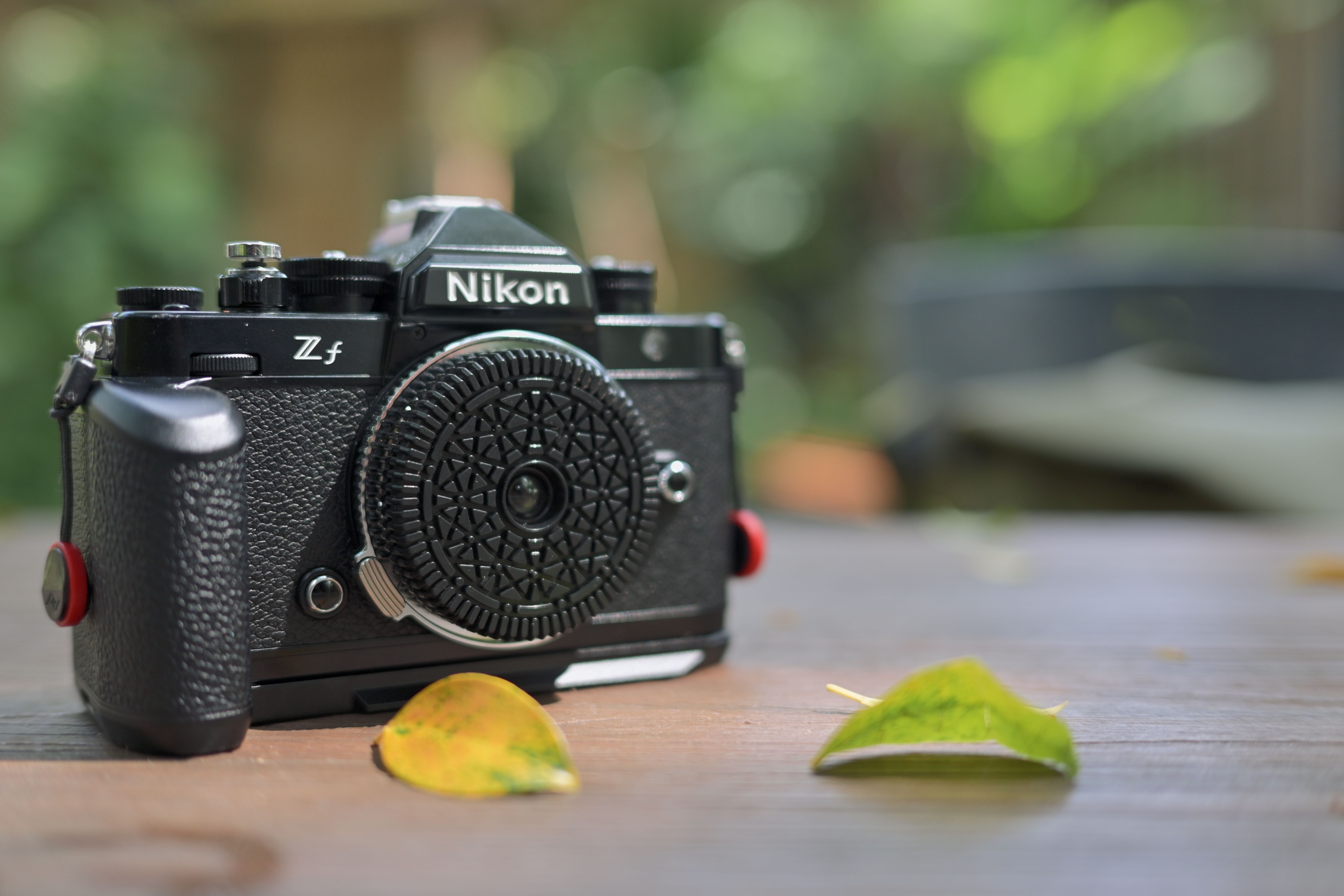 Close-up of a vintage style camera on a wooden table with leaves around. Natural outdoor setting.