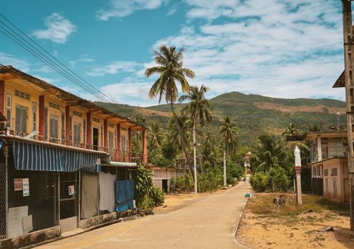 Free Scenic view of a Vietnamese village street lined with palm trees and traditional buildings in Quy Nhơn Nam, Gia Lai. Stock Photo