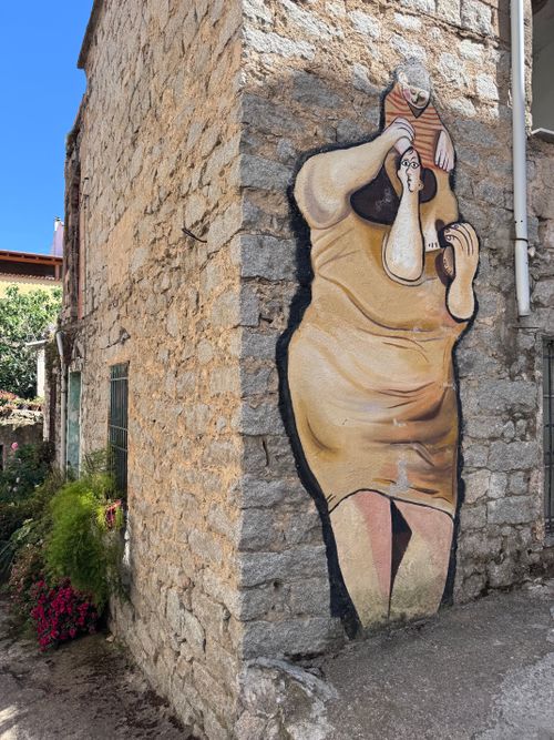 Free Colorful street art mural adorns a rustic stone wall outdoors in Sardinia under a bright blue sky. Stock Photo