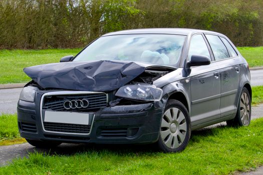 A damaged Audi car with a crumpled front end parked on the side of the road after a crash.
