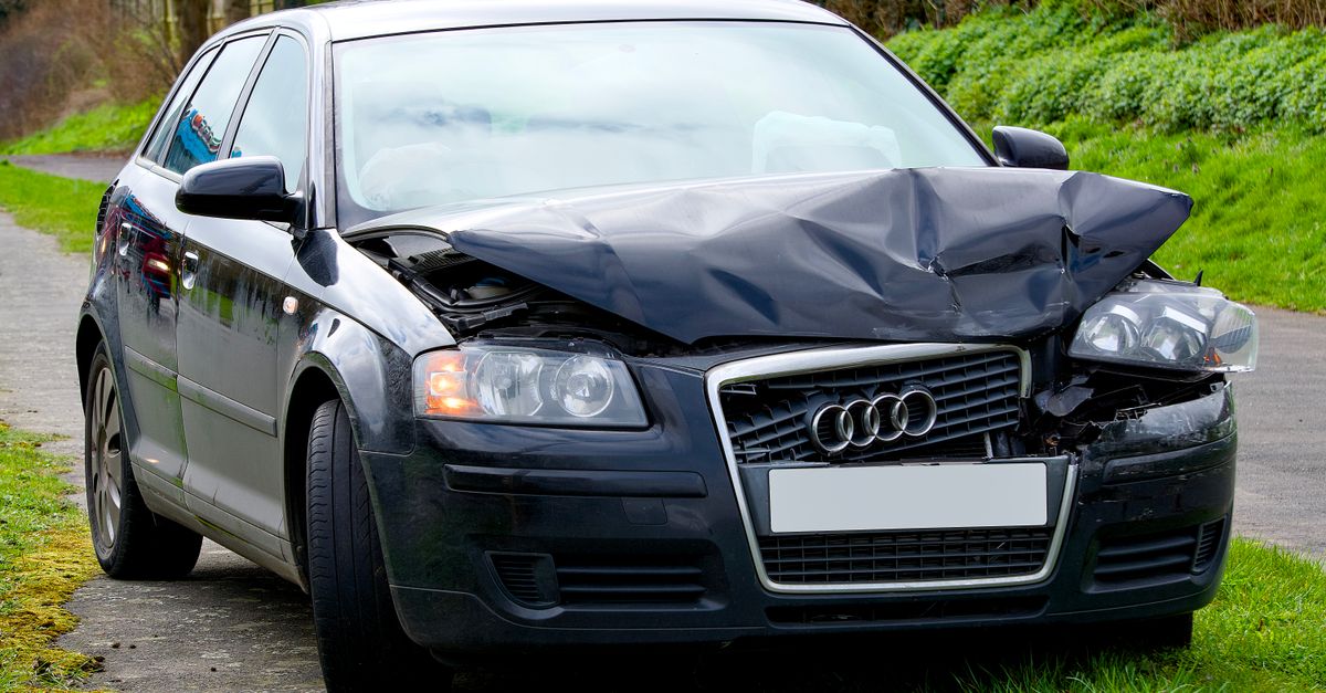 Front view of an Audi car with severe damage from a road collision, parked outdoors.