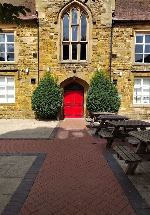 Free A historic stone building with a bright red door and picnic tables under the sunlight. Stock Photo