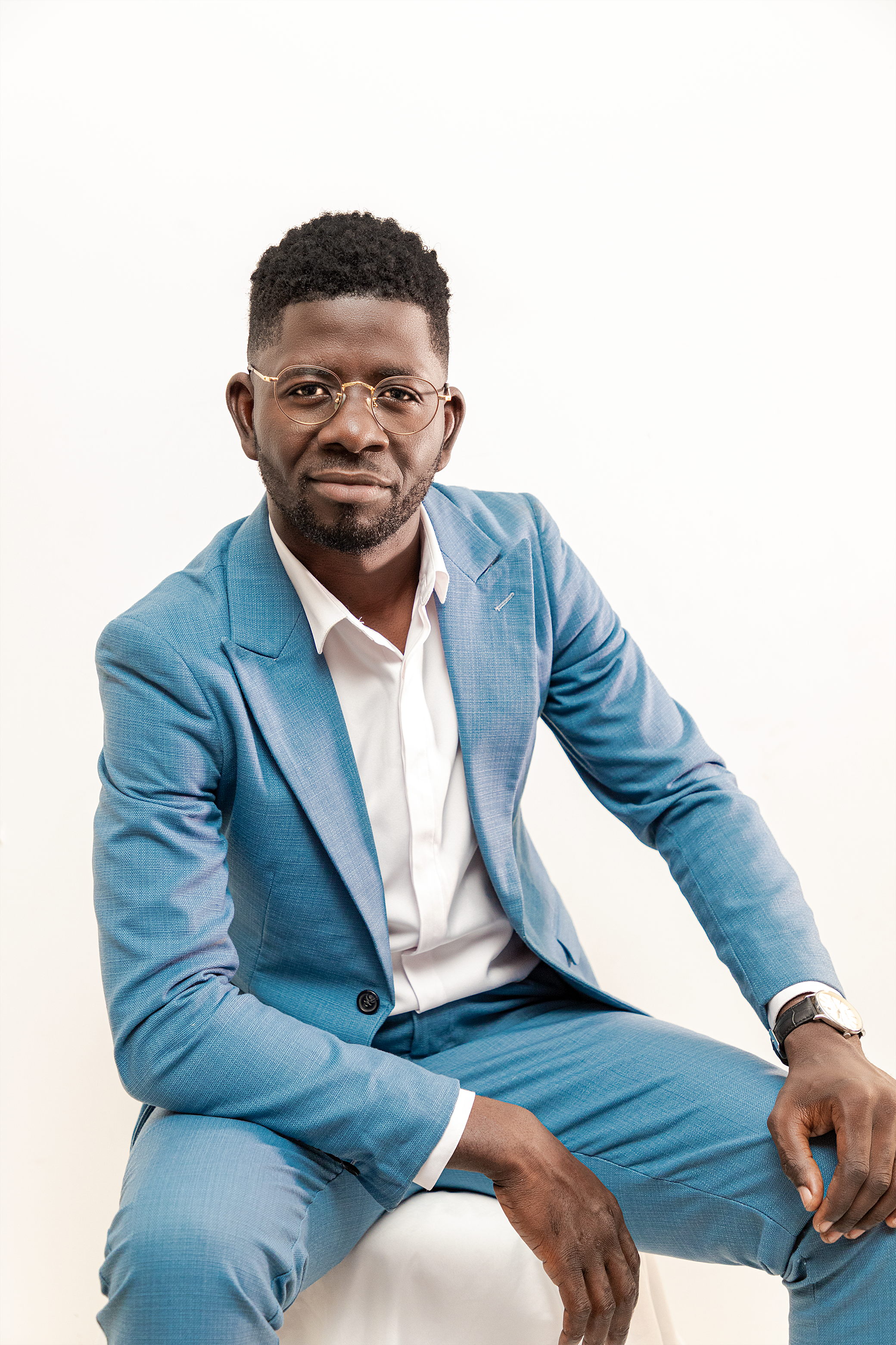 Portrait of a confident African man in a blue suit, seated against a white background, projecting professionalism and style.