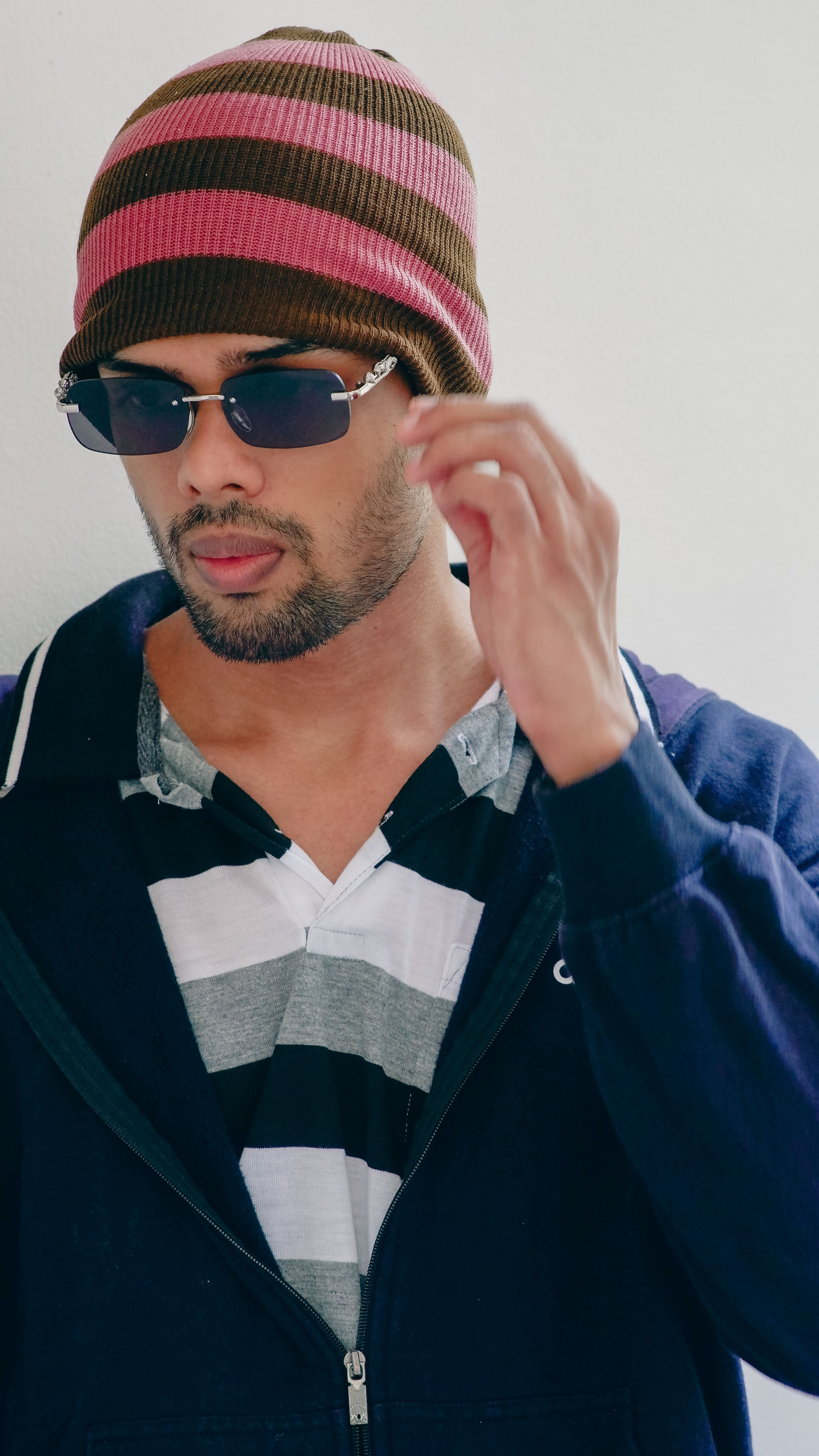 Fashionable adult wearing sunglasses and a striped beanie, exuding modern style and coolness.