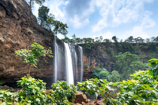 在明亮的蓝天下，宁静的瀑布倾泻而下，周围环绕着郁郁葱葱的绿色植物