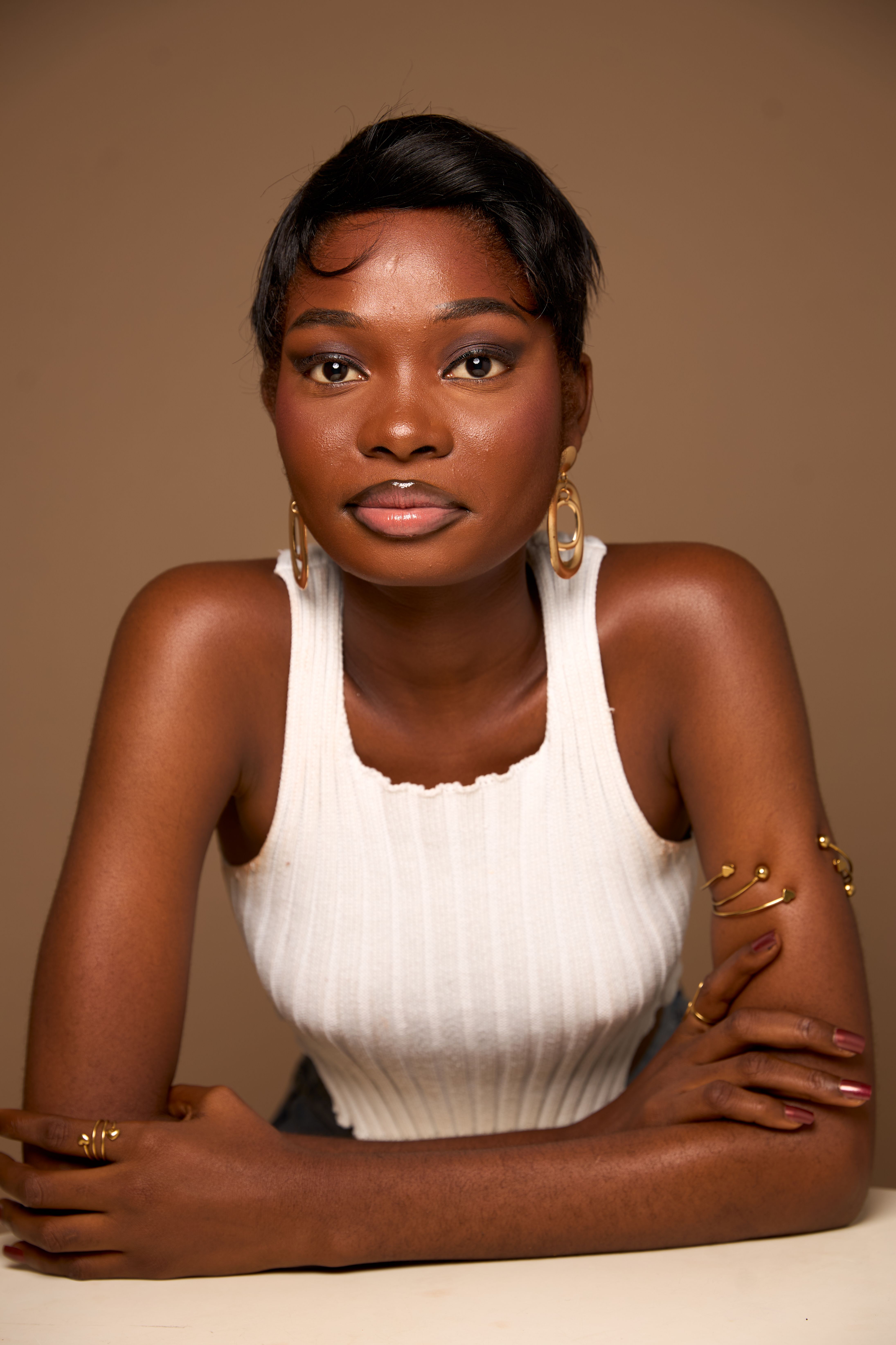 Stylish portrait of an elegant young woman with jewelry, wearing a white tank top against a neutral background.