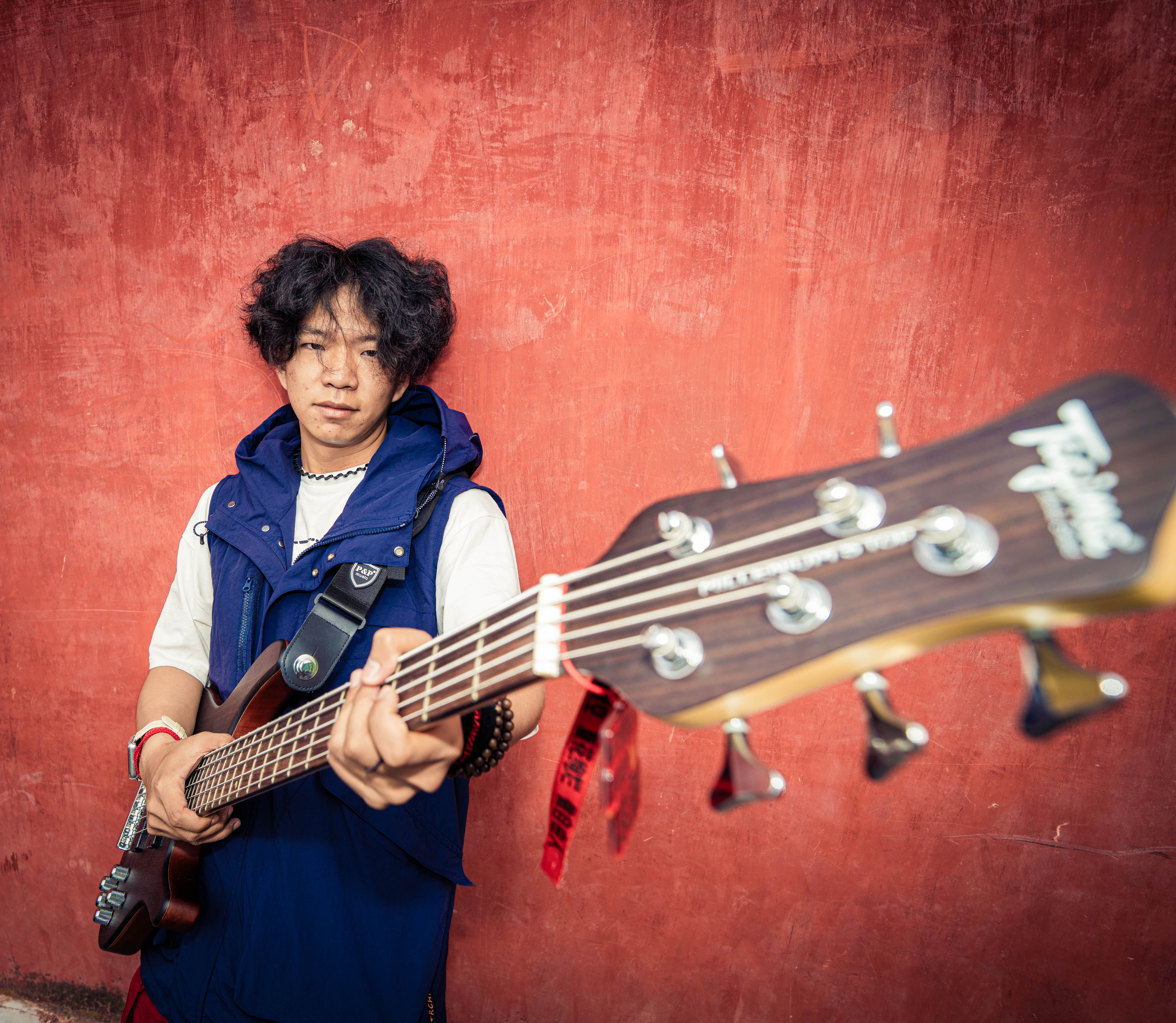Young musician holding a bass guitar with focus on strings and vibrant background.