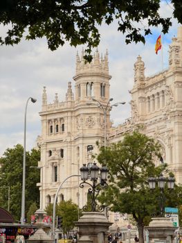 Cibeles Palace in Madrid with the Spanish flag, trees, and classic architecture.