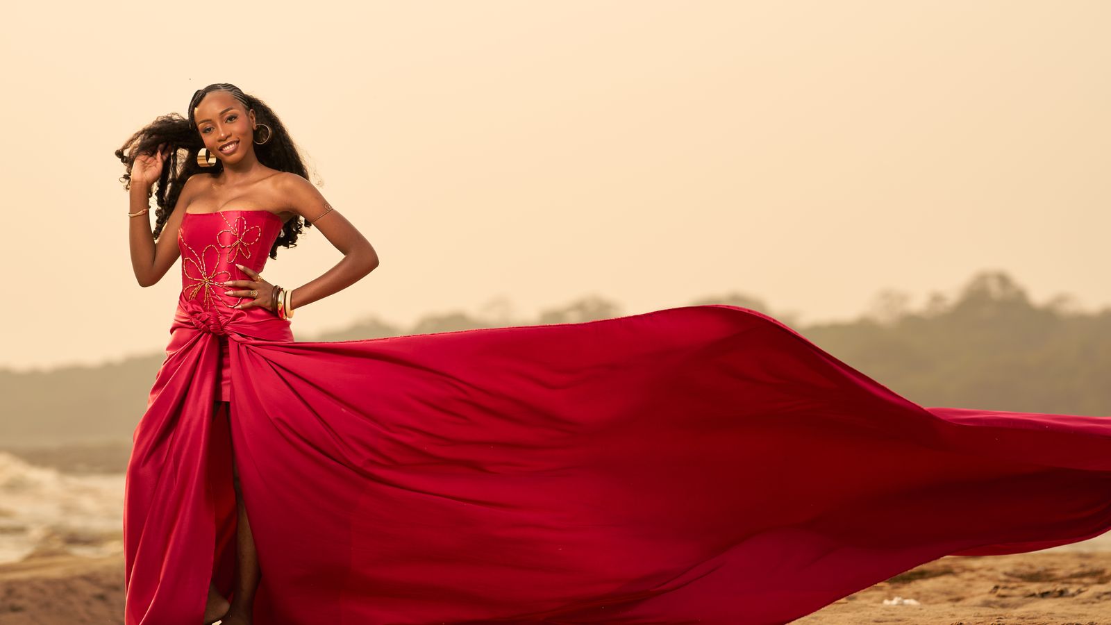Elegant woman in flowing red gown on beach, Gabon