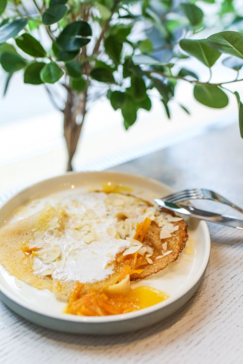 Free White ceramic plate with fresh tasty pancakes with sauce for breakfast served on wooden table with fork and knife in light room Stock Photo