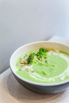 Creamy broccoli soup garnished with seeds and swirls of cream in a bowl.