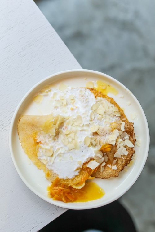 Free Top view of white plate with fresh tasty crepes with orange jam and almond flakes served on plate on edge of wooden table in light room Stock Photo